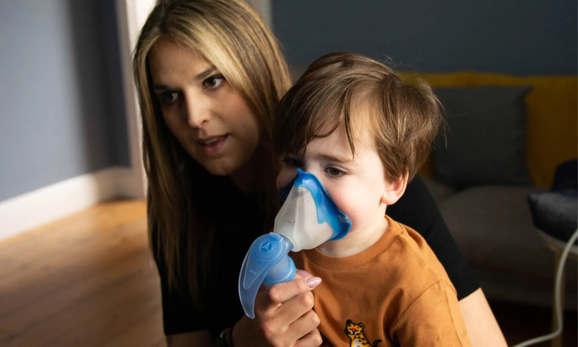 A photo of a woman and boy. The woman is low in the picture so her head is a similar level to the boy. The boy has a ventilation mask held to his face.